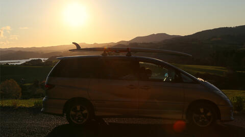 Campervan with surfboard on the roof, sunset and rolling hills in the background