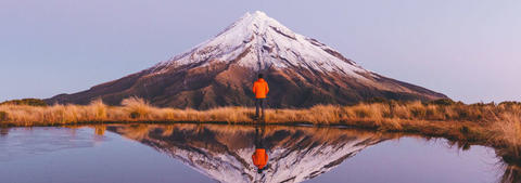 Man standing by NZ snow-capped Mount Taranaki and lake