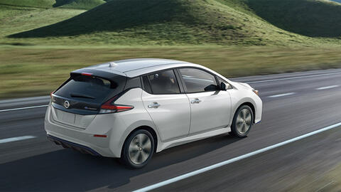 White Nissan Leaf driving past green hills