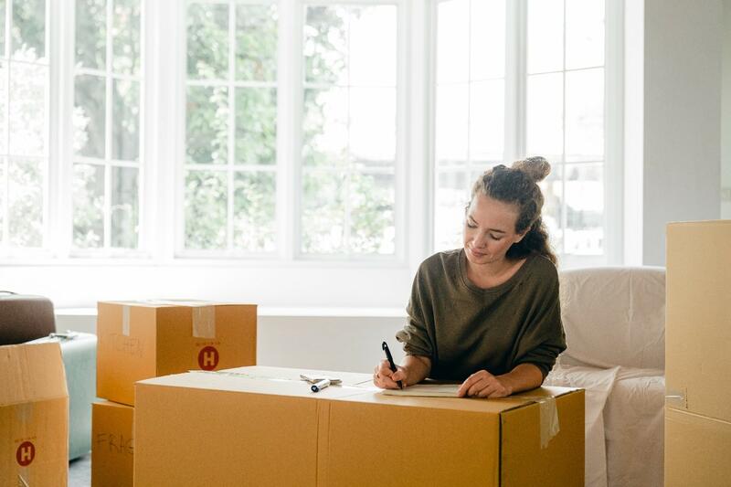 Woman writing on a cardboard moving box in a living room